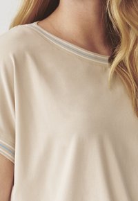 Beige t-shirt med korte ærmer, der har en blød tekstur og en farvet stribet halsudskæring i blå og hvid. Enkel, afslappet pasform.