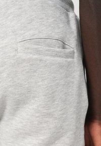 Graue Baumwollschweißhose mit einer kleinen, flachen Tasche an der Seite. Die Textur ist glatt mit einem subtilen melierten Muster.