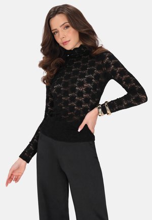 Top lungo a maniche in pizzo nero con motivo floreale, collo alto e orlo a costine. Abbinato a pantaloni neri a vita alta.