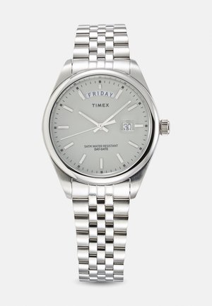 Zilveren roestvrijstalen horloge met een ronde grijze wijzerplaat, zilveren uurmarkeringen, dag- en datumaanduiding, en een schakelarmband.