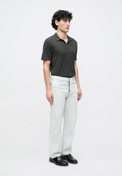 Γκρι κοντομάνικο πόλο πουκάμισο συνδυασμένο με ανοιχτό μπλε τζιν παντελόνι με ίσια γραμμή και μαύρα επίσημα παπούτσια. Το μοντέλο στέκεται σε ουδέτερο φόντο.