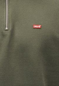 Ύφασμα ελιάς με μεταλλικό φερμουάρ και μικρό κόκκινο λογότυπο Levi's στο στήθος.