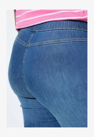 Gros plan sur une personne portant un jean en denim bleu et une chemise rayée rose et blanche, mettant l'accent sur la taille et la zone des hanches.