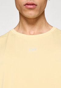 Ανοιχτό κίτρινο μπλουζάκι με στρογγυλή λαιμόκοψη και κοντά μανίκια. Διαθέτει διακριτικό λευκό λογότυπο στο κέντρο. Μαλακή, απαλή υφή υφάσματος.