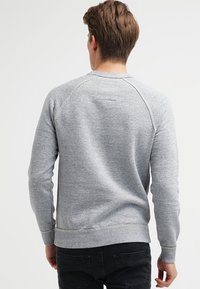 Felpa grigia con un tessuto testurizzato, maniche raglan e orlo a coste. Design semplice senza fantasie o brand visibili sul retro.