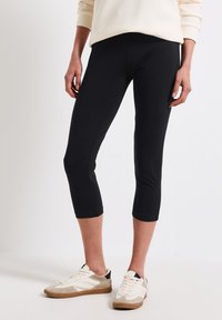 Svarta capri leggings i stretchigt material, med en åtsittande design och en mjuk textur. Matchas med vita och beige sneakers.