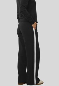 Svarta sweatpants i mjukt material, med ett brett vitt sidoremsa. Passformen är avslappnad, med fickor och en slät yta.