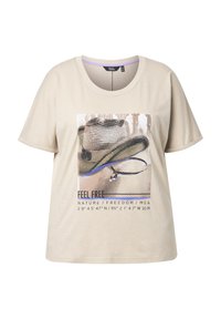 Camisa de manga corta beige con un gráfico de un sombrero de vaquero y texto que dice "SIENTE LIBRE NATURA / LIBERTAD / YO &" y coordenadas geográficas.