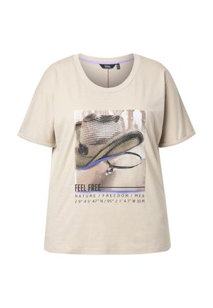 Beige shirt met korte mouwen, bedrukt met een cowboyhoed grafiek en tekst die luidt "BE FREE NATURE / FREEDOM / ME &" en geografische coördinaten.