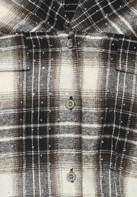 Sort-hvidt ternet button-up skjorte med krave, der har to brystlommer og en tekstureret overflade. Knapperne er cirkulære med blomsterdesigns.