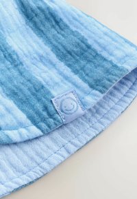 Svetlo modro blago z vzorcem gradienta, z mehko teksturo in našitim šivom z nalepko nasmejanega obraza na robu.