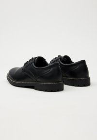 Zapatos de cuero negro con una textura suave, con punta redondeada, cierre con cordones y una suela gruesa y resistente de goma.