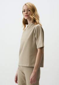 Top in maglia a coste beige con maniche corte e scollatura alta. Il tessuto ha una texture sottile, abbinato a un fondo a coste coordinato.