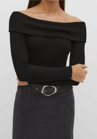 Zwarte geribde off-shoulder top met lange mouwen, gecombineerd met een donker denimrok en een zilveren riem met ovale gesp.