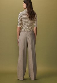Top ajustat, cu dungi, și mâneci cu margini ondulate, purtat cu pantaloni largi, cu talie înaltă, dintr-un material texturat, de culoare bej deschis.
