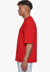Camiseta de algodón roja con un corte relajado, escote redondo y mangas cortas. Presenta un pequeño detalle de logo en la manga y un diseño liso.