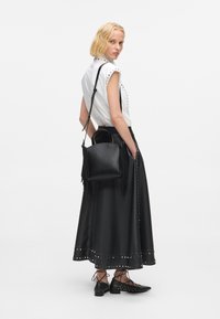 Fekete bőr, bojtokkal díszített kézi táska, állítható pánttal, amit egy fényes fehér inggel párosítanak, amely szegecsekkel van díszítve, és egy fekete bőr szoknyával.