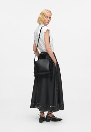 Geantă de umăr din piele neagră cu franjuri, cu mânere superioare și curea ajustabilă, asortată cu o cămașă albă cu detalii cu capse și o fustă din piele neagră.