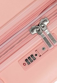 Rosa Hartschalenkoffer mit zwei Metallreißverschlüssen, Zahlenkombinationsschloss und strukturiertem Oberflächenfinish. Die Reißverschlüsse haben ein glattes, metallisches Finish.