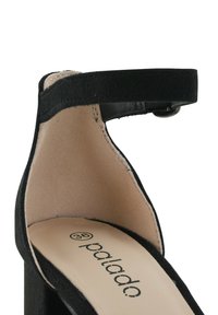 Scarpa alta in suede nera con cinturino alla caviglia. L'interno presenta una fodera beige liscia e un logo impresso. Design classico del tacco.