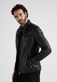 Zwarte leren jas met een slim fit ontwerp, ritssluitingen, gestructureerde schouderaccenten en een staande kraag. Vloeiend afwerking en op maat gemaakte silhouet.