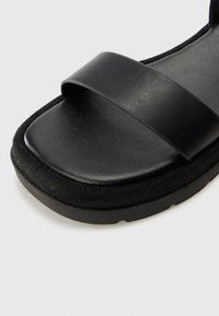 Sandale noire avec deux larges brides en cuir, une semelle intérieure texturée et une épaisse semelle en mousse pour plus de confort. Design à bout rond.