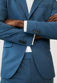 Blaues Sakko mit glatter Textur; verfügt über vier schwarze Knöpfe an den Manschetten und eine weiße Manschette darunter. Taillierte Passform mit scharfen Revers.