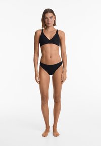 Črn bikini komplet, ki vključuje vrhnji del z v-izrezom in širokimi naramnicami ter nizkimi hlačkami, izdelan iz teksturiranega materiala.