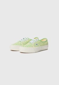 Green canvas sneakers with a zebra stripe pattern, white laces, and a cream rubber sole, featuring a blue logo tag on the side.