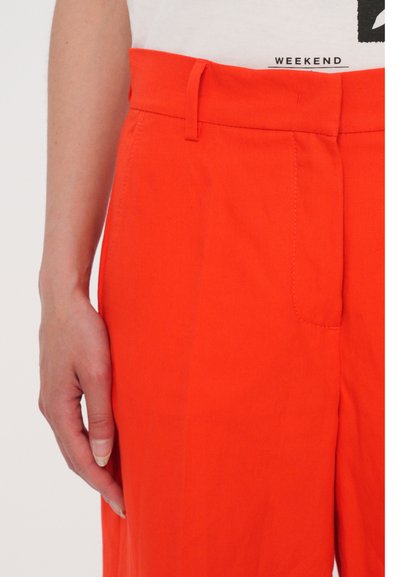 Lys orange bukser med en glat tekstur, der har en tætsiddende talje, bæltesløjfer og en sidelomme.