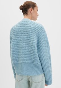 Maglione lavorato a maglia blu chiaro con un design testurizzato a coste, caratterizzato da spalle cascanti e un orlo ampio. Materiale morbido e soffice.