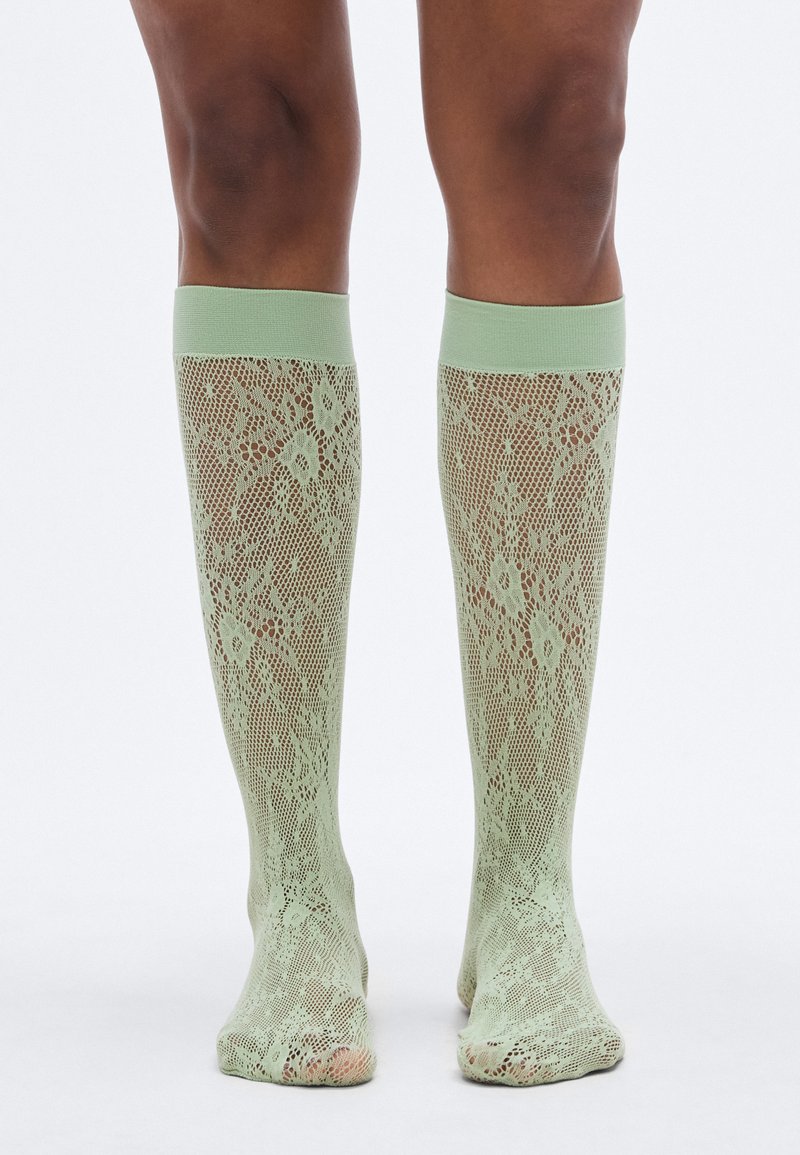 Svijetlozelene čarape do koljena od čipke s cvjetnim uzorkom i jednobojnim, teksturiranim obrubom na vrhu.