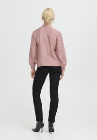 Hellrosa Bluse mit langen Ärmeln aus strukturiertem Stoff, lockere Passform und elastischen Bündchen, kombiniert mit schwarzen, enganliegenden Hosen und patentierten Ankle Boots.