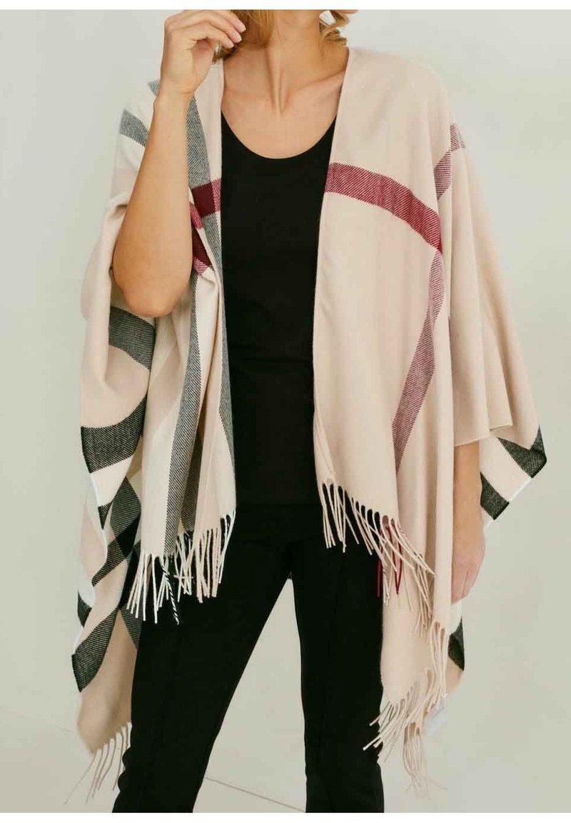 Châle beige avec de larges rayures noires et rouges et des bords à franges, drapé sur une personne portant un haut et un pantalon noirs.