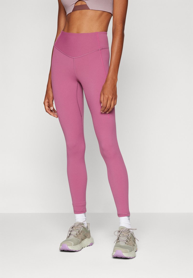 Hoch taillierte Leggings aus einem weichen rosa Stoff, mit kontrastierenden Nähten und einem eleganten, figurbetonten Design. Kombiniert mit neutralen Sneakers.