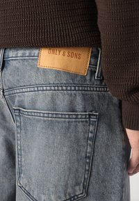 Heledad teksad, millel on hele pesu, ja nahktagi, millel on kirjas "ONLY & SONS." Klassikaline viie tasku disain koos nähtavate õmblusdetailidega.