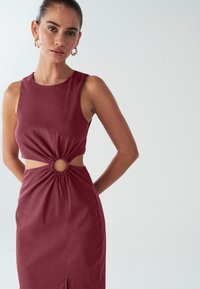 Bordové šaty s priliehavým živôtikom, výrezmi po bokoch a kruhovým detailom v páse, vyrobené z hladkej, jemnej tkaniny.