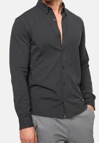 Harmaa pitkähihainen paita kevyestä kankaasta, jossa on kaulus, nappikiinnitys edessä ja rento istuvuus, yhdistetty harmaisiin housuihin.