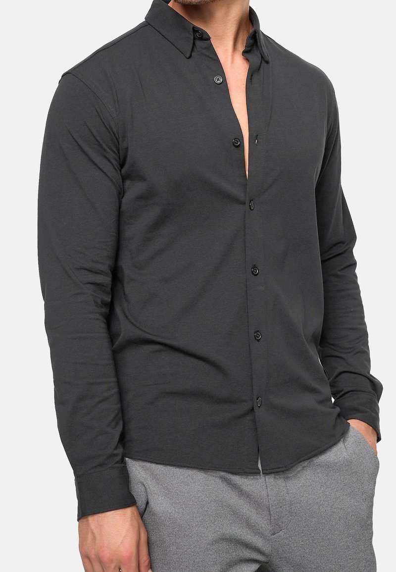 Harmaa pitkähihainen paita kevyestä kankaasta, jossa on kaulus, nappikiinnitys edessä ja rento istuvuus, yhdistetty harmaisiin housuihin.