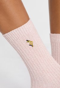 Calcetines rosas de canalé con un diseño floral bordado en verde y amarillo. Textura suave, de longitud hasta el tobillo y con un ajuste ceñido.