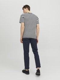 Gestreiftes Kurzarm-T-Shirt mit dunkelblauen und weißen Streifen, kombiniert mit dunkelblauen Chinos und schwarzen Schuhen, von hinten betrachtet.