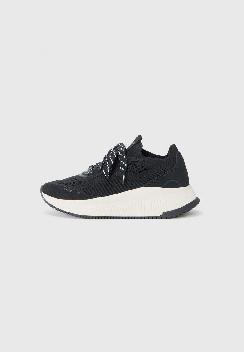 Black athletic sneaker with textured mesh upper, contrasting white midsole, and patterned black laces. Side logo detail present.