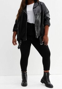 Czarna skórzana kurtka motocyklowa z srebrnymi suwakami, połączona z białym T-shirtem w paski i czarnymi obcisłymi dżinsami. Czarne sznurowane buty bojowe.