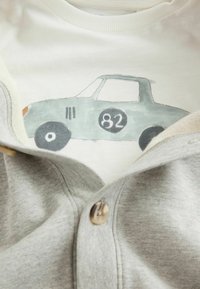 Grijze cardigan met knoopdetails, over een witte T-shirt met een groene geïllustreerde auto met het nummer 82 op de zijkant.
