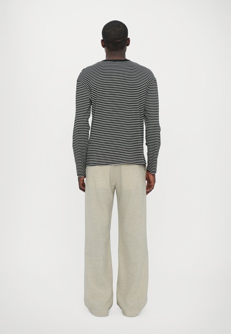 Schwarz-weißer gestreifter Langarmshirt mit rundem Halsausschnitt, kombiniert mit hellgrauen weit geschnittenen Hosen aus einem strukturierten Stoff.