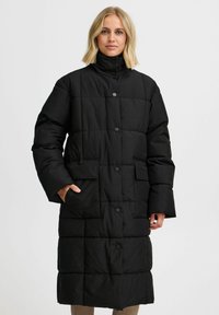 Melna gara pūka jaka ar augstu apkakli, kas raksturojas ar quilted dizainu, spiedpogām un divām priekšējām kabatām. Visā virsmā gluda tekstūra.