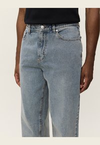 Light blue denim jeans with a loose fit. Features a classic five-pocket design and visible stitching. Buttons and zipper at the waist.