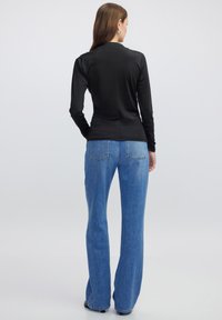 Schwarzes Langarmoberteil mit taillierter Passform, kombiniert mit hochgeschnittenen, hellblauen Schlagjeans. Das Outfit zeichnet sich durch eine glatte Textur und minimales Design aus.