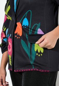 Schwarze Blumensakko mit lebhaften Blumen in Orange, Pink, Blau und Grün, austexturiertem Stoff und einem dekorativen rosa Saum.