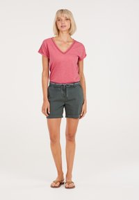 Rode V-hals T-shirt gecombineerd met donkergroene shorts met een drawstring taille en opgerolde mouwen, aangevuld met bruine slippers.